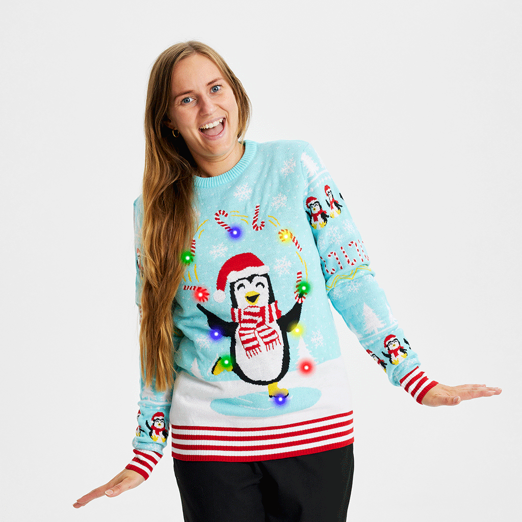 Une femme portant un pull de Noël bleu clair avec des pingouins et des lumières.